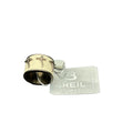 Primo piano di un anello da uomo Breil Stones mostrato da un'angolazione inclinata. Il gioiello presenta una fascia centrale in ecopelle o texture nido d'ape color crema, decorata con tre croci stilizzate. La montatura è in acciaio color bronzo con interno liscio visibile. Sullo sfondo, l'etichetta originale Breil Stones grigia su sfondo bianco.