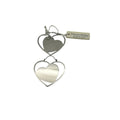 Coppia di orecchini a monachella Nomination mostrati in verticale su sfondo bianco. Ogni orecchino presenta un design a doppio cuore concentrico in acciaio lucido, con un cuore pieno inscritto in una sagoma a cuore vuota. In alto a destra, l'etichetta originale beige con la scritta 'Nomination Made in Italy' legata con un cordoncino bianco.