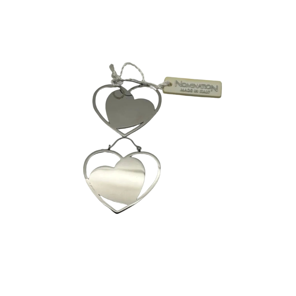 Coppia di orecchini a monachella Nomination mostrati in verticale su sfondo bianco. Ogni orecchino presenta un design a doppio cuore concentrico in acciaio lucido, con un cuore pieno inscritto in una sagoma a cuore vuota. In alto a destra, l'etichetta originale beige con la scritta 'Nomination Made in Italy' legata con un cordoncino bianco.
