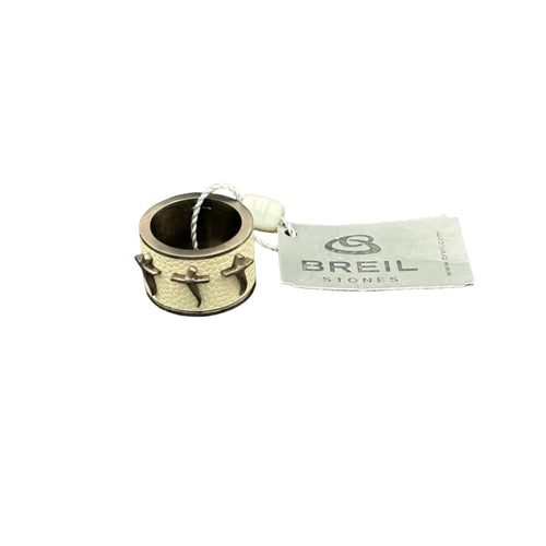 Vista dall'alto di un anello a fascia da uomo della collezione Breil Stones. L'immagine offre una panoramica della forma circolare perfetta dell'anello, mettendo in evidenza la texture a nido d'ape color beige della fascia centrale e le tre croci posizionate in sequenza. La struttura è in acciaio color bronzo, mostrata insieme all'etichetta del marchio e al sigillo di garanzia bianco.