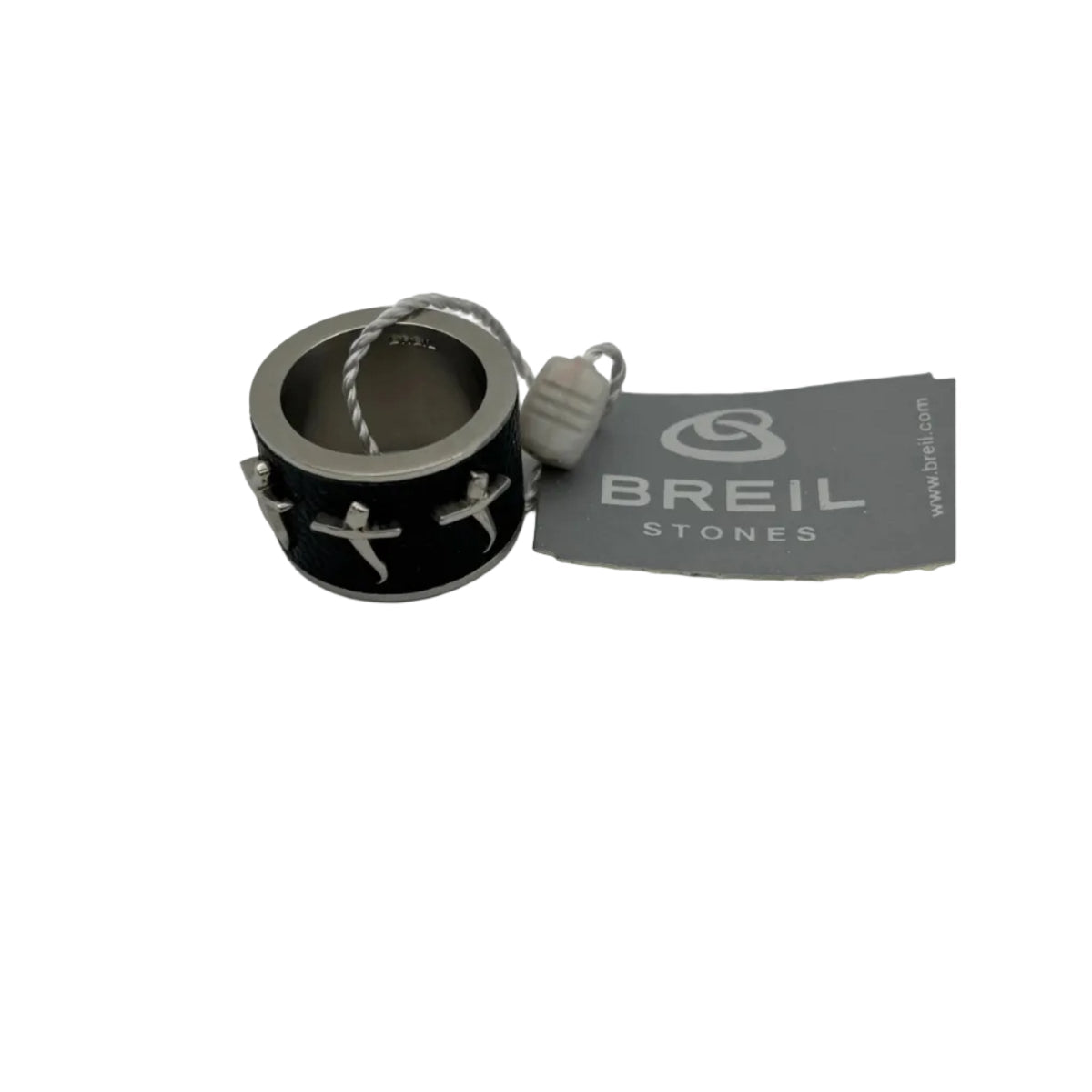 Vista dall'alto di un anello a fascia da uomo della collezione Breil Stones. L'immagine offre una panoramica della forma circolare perfetta dell'anello, mettendo in evidenza la texture a nido d'ape color nero della fascia centrale e le tre croci posizionate in sequenza. La struttura è in acciaio color argento, mostrata insieme all'etichetta del marchio e al sigillo di garanzia bianco.