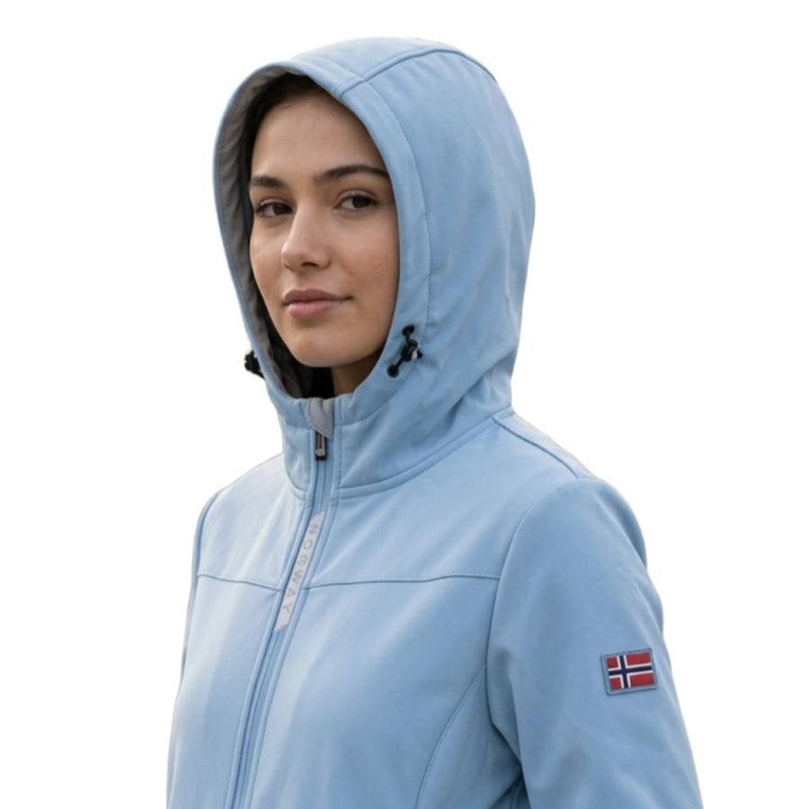 Primo piano di una modella che indossa una giacca sportiva azzurro chiaro con cappuccio sollevato. La giacca presenta una chiusura a zip centrale con la scritta 'NORWAY' lungo il bordo e una piccola toppa sulla manica sinistra che raffigura la bandiera norvegese. Lo sfondo è bianco e neutro."