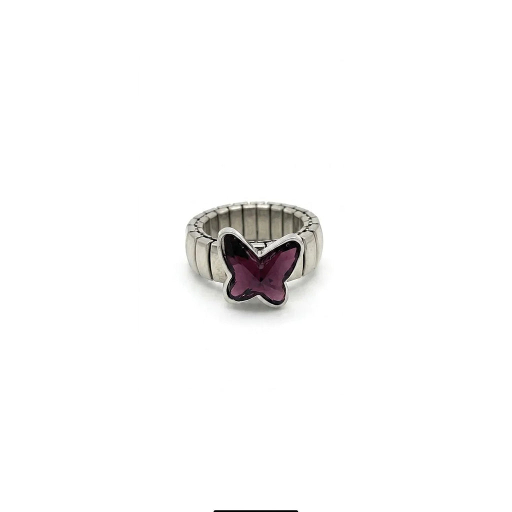 Primo piano di un anello elastico con maglie piatte in acciaio e decorazione centrale a forma di farfalla in vetro sfaccettato viola scuro, isolato su sfondo bianco.