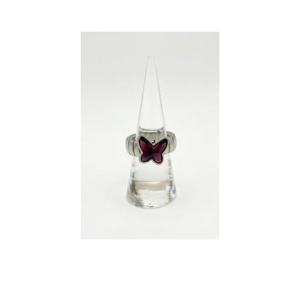 Anello a fascia elastica in metallo argentato con farfalla in cristallo viola ametista, esposto verticalmente su un supporto a cono trasparente su sfondo bianco uniforme.