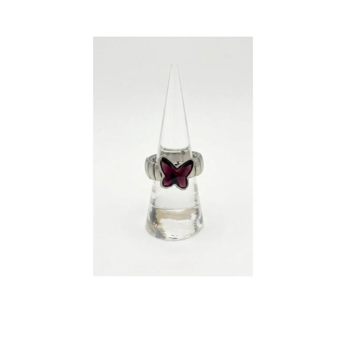 Anello a fascia elastica in metallo argentato con farfalla in cristallo viola ametista, esposto verticalmente su un supporto a cono trasparente su sfondo bianco uniforme.